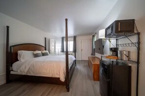 Une chambre à coucher avec un lit à baldaquin, un banc en bois, une télévision et une étagère intégrée où se trouve une machine à café.
