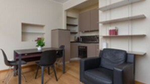 Una sala de estar moderna con un sofá de cuero negro, una mesa de comedor con sillas y estanterías empotradas con libros y objetos decorativos.