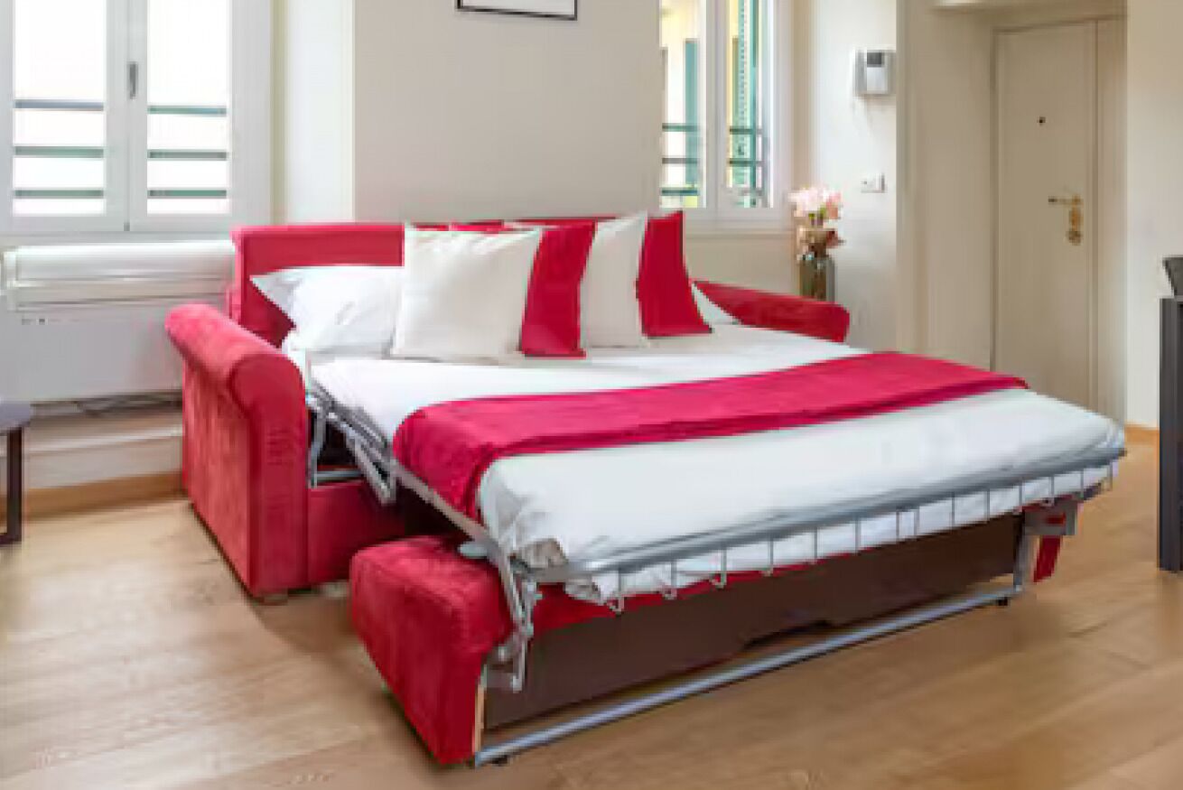 Un lit avec une couvre-lit rouge et blanche, une tête de lit rouge et une table de chevet avec une lampe.