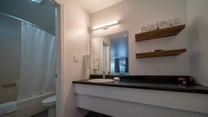 Ein modernes Badezimmer mit einem weißen Waschbecken, einem Spiegel und Holzregalen darüber.