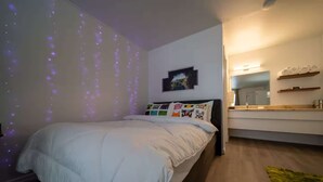 A bedroom with a bed, a nightstand, a bedside table, a mirror, and a wall-mounted shelf.