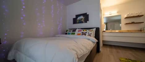 Un dormitorio con cama, mesita de noche, espejo y estante en la pared.
