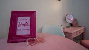 A pink-framed picture with text, a pair of heart-shaped sunglasses, a vanity with a mirror, and a pink chair. - Pink Room, #16 at Glory Dayz! (Eureka Springs)