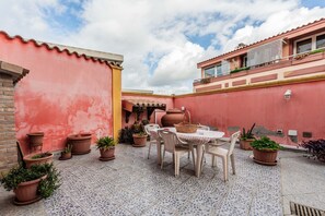 Une terrasse avec une table et des chaises, entourée de plantes en pot et d’un mur rouge.