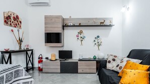 Ett modernt vardagsrum med en svart soffa, ett TV-bord i trä, en öppen spis och ett konstverk som hänger på väggen.
