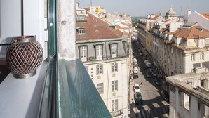 Vista desde una ventana sobre una calle con edificios y cielo despejado.