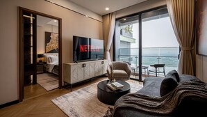 Una sala de estar moderna con un televisor grande, un sofá, una mesa de centro y vistas de la ciudad a través de amplias ventanas.