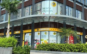 A modern building with a curved glass facade, featuring advertisements for a store named 'Farmers' that sells fresh meat, seafood, and dairy products. - The Parkland Lux & Easy in East Tower (Ho Chi Minh City)