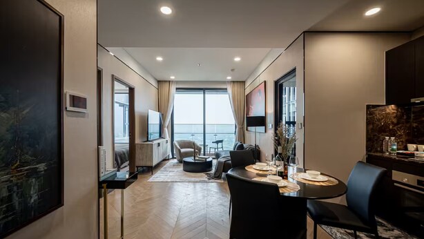 Una habitación de hotel moderna con un ventanal grande, un comedor con una mesa redonda y un conjunto de asientos.