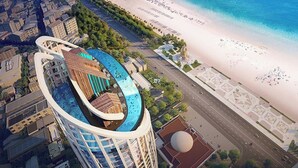 Ein Hochhaus mit gewölbter Dachlinie, einem Swimmingpool und Blick auf den Strand.