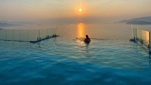 Eine Person in einem klaren, blauen Infinity-Pool mit Blick auf den Sonnenuntergang über dem Wasser.