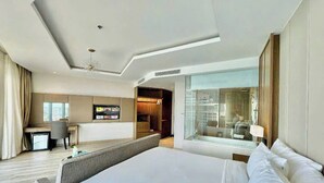 Ein modernes Hotelzimmer mit einem großen Bett, einem Schreibtisch und einem durch eine Glastrennwand einsehbaren Badezimmer.