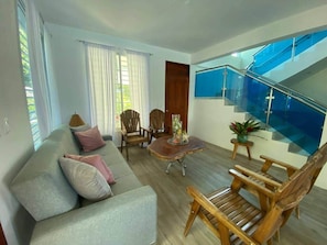 A modern living room with a sofa, chairs, a coffee table, and a staircase with glass railings.