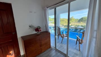 Una habitación con un aparador de madera, puerta de vidrio que da a un balcón con piscina y sillas.
