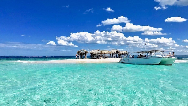 Ein Strand mit klarem türkisblauem Wasser, einem Boot und einer Struktur mit Reetdächern.