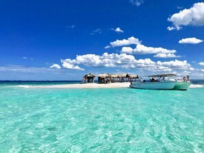 Une plage avec une eau turquoise et limpide, un bateau et une construction surmontée de toits de chaume.