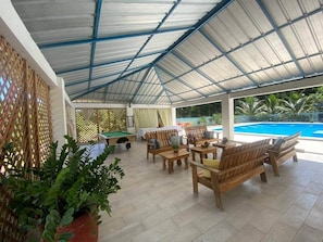 Ein überdachter Außenbereich mit Holzmöbeln, einem Pool und Topfpflanzen.