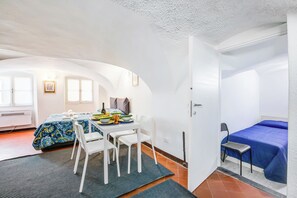 Une chambre à coucher de taille réduite, comprenant un lit, une table à manger avec des chaises et un petit coin cuisine.