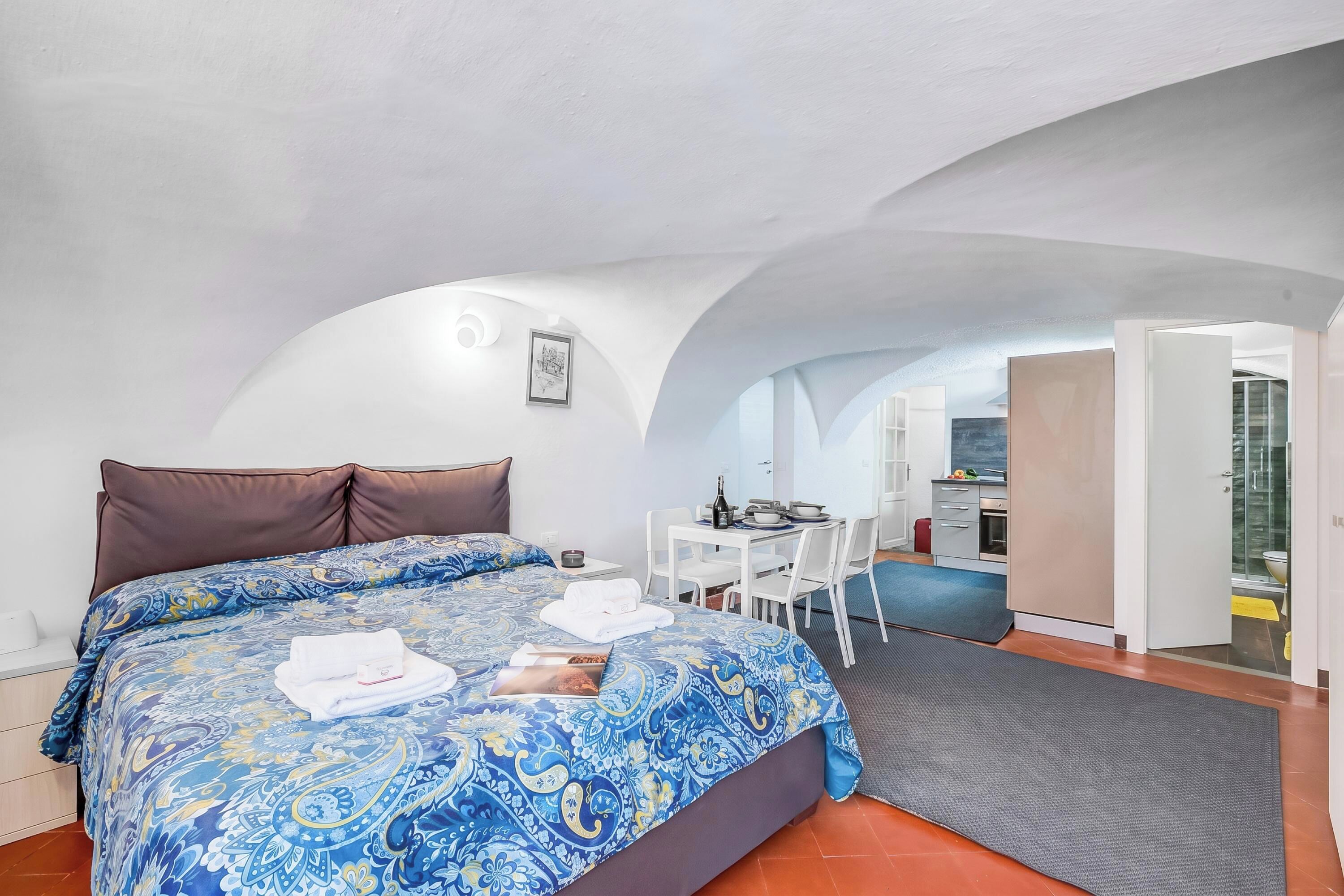 A bedroom with a bed, a desk, and a kitchenette.