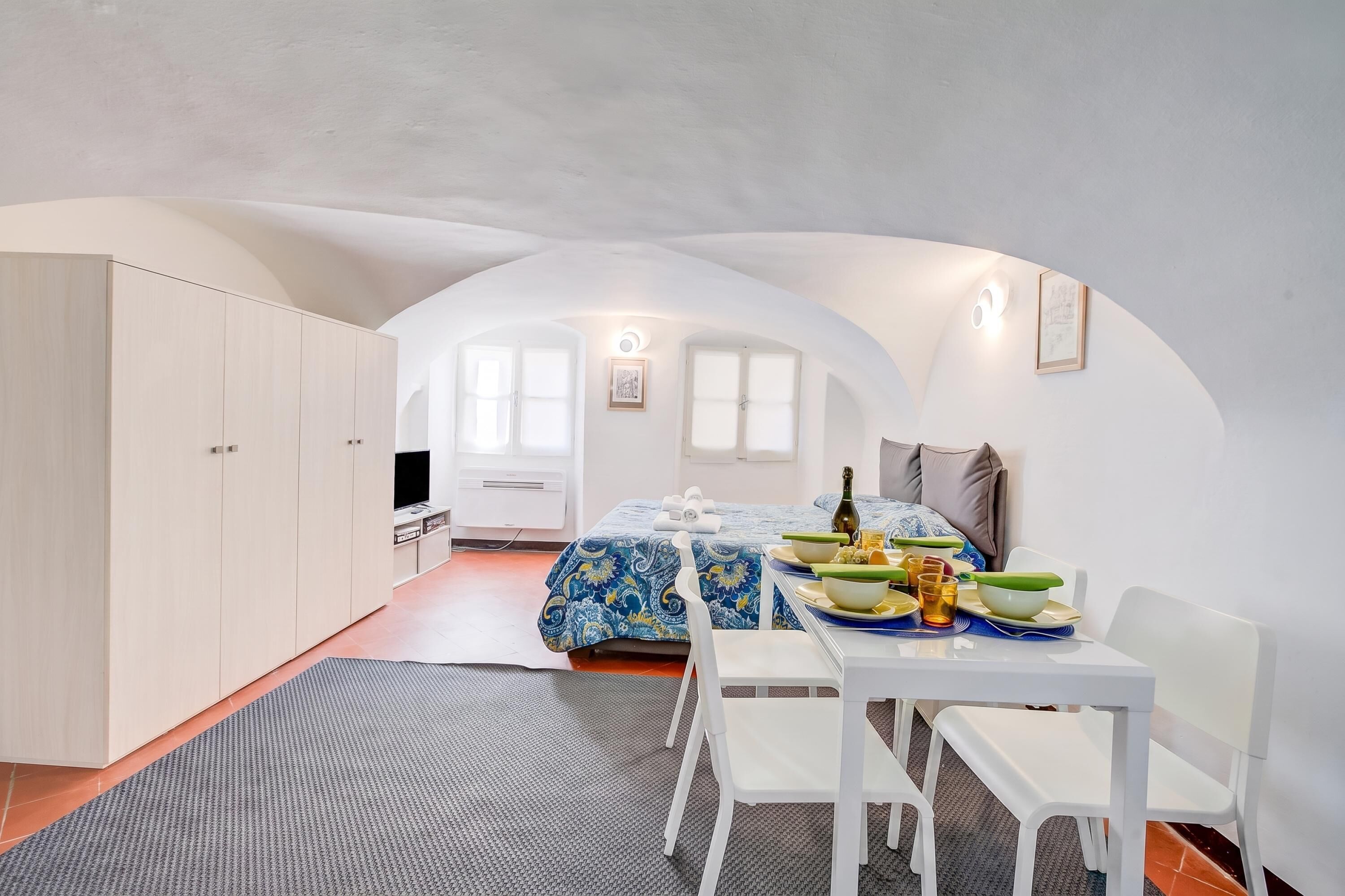 A compact room with a bed, a dining table with chairs, a television, and a wardrobe.