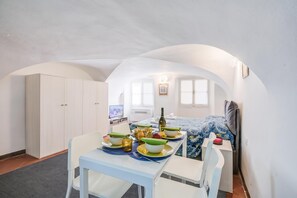 A compact room with a dining table set for two, a bed with a patterned bedspread, a television, and a wardrobe. - Casa Vacanze Maimone 3 Central Sanremo Old Town (Sanremo)