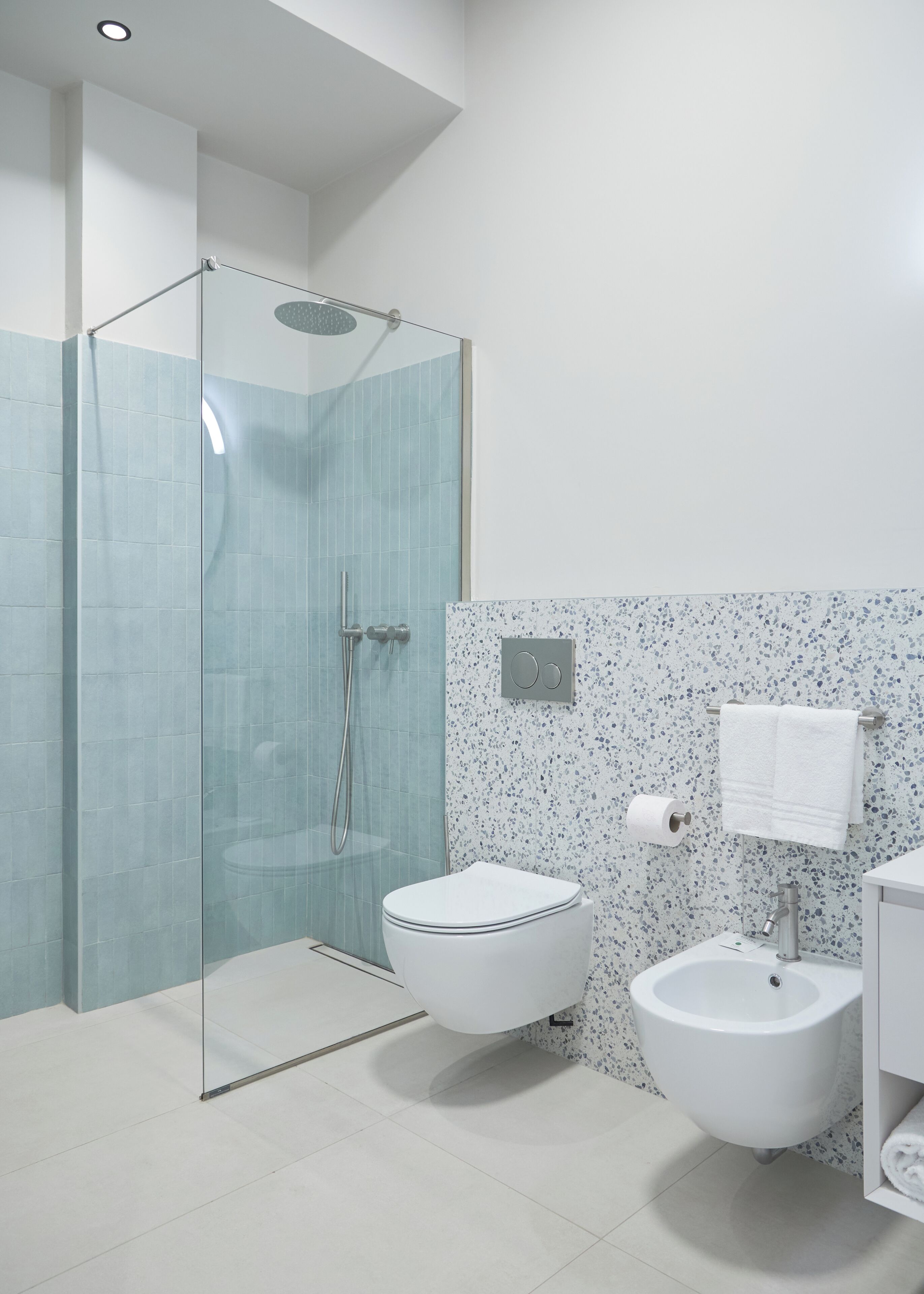 Egy modern fürőszoba üveg válaszfallal ellátott zuhanyzóval, WC-vel, bidével és mosdókagylóval.