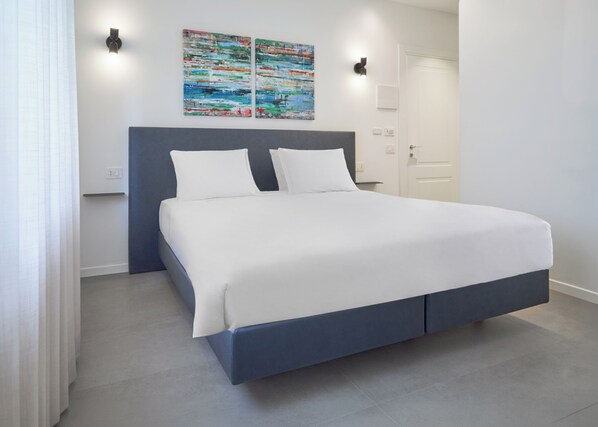 A modern bedroom with a large bed, two wall-mounted light fixtures, and a colorful abstract painting above the bed. - DoorMI - Premium Suites and Apartments (Milan)