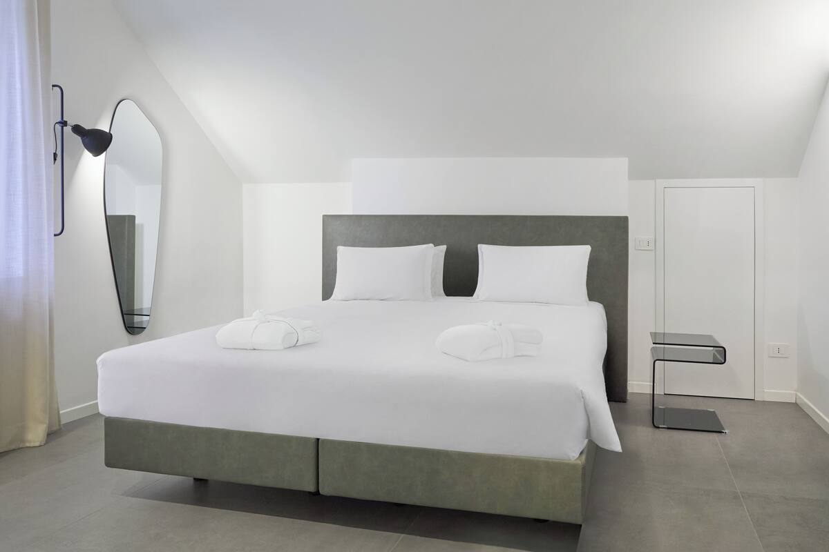 Una habitación de hotel moderna con una cama grande, una mesita de noche, un espejo y una puerta.