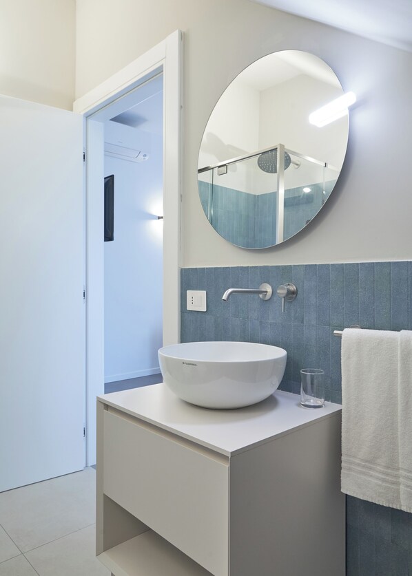 A modern bathroom with a white sink, a round mirror, and a towel rack.