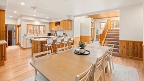 Une cuisine spacieuse avec des meubles de rangement en bois, un coin repas doté d’une grande table et de chaises, et un escalier menant à l’étage supérieur.
