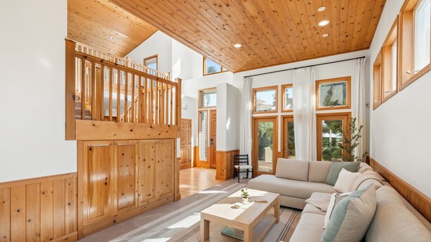 Un vaste espace de vie doté d’un plafond en bois, de grandes fenêtres et d’un canapé intégré.