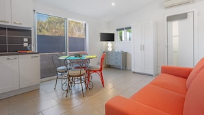 A modern kitchen with white cabinets, a dining table with chairs, a TV, and an orange sofa. - Apartment 'Les Sables' with Private Terrace, Wi-Fi and Air Conditioning (Bormes-les-Mimosas)