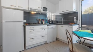 A modern kitchen with white cabinetry, a built-in microwave, and a dining area with a table and chairs. - Apartment 'Les Sables' with Private Terrace, Wi-Fi and Air Conditioning (Bormes-les-Mimosas)