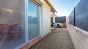 A covered patio area with a sliding glass door, wooden flooring, and outdoor furniture. - Apartment 'Les Sables' with Private Terrace, Wi-Fi and Air Conditioning (Bormes-les-Mimosas)