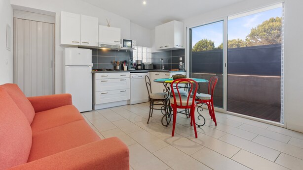 A modern kitchen with white cabinets, a dining table with red chairs, and a large sliding glass door to the outside. - Apartment 'Les Sables' with Private Terrace, Wi-Fi and Air Conditioning (Bormes-les-Mimosas)