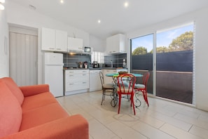 A modern kitchen with white cabinets, a dining table with red chairs, and a large sliding glass door to the outside.