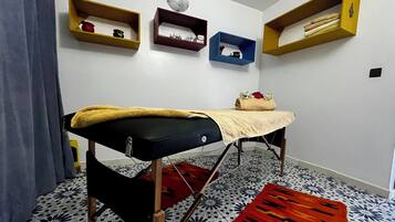 Quarto com mesa de massagem, ladrilhos estampados e prateleiras fixas na parede com diversos objetos.