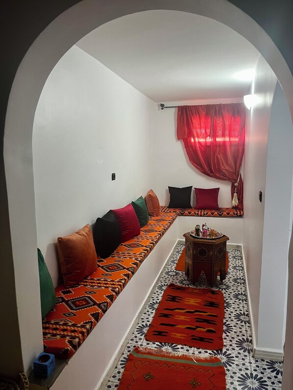 Ein gemütlicher Sitzbereich mit einem gemusterten Sofa, einem kleinen Tisch und einem roten Vorhang.