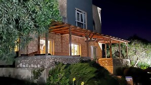 Een tweelaags huis met een stenen gevel, een houten pergola en een kleine tuin met een zwembad.