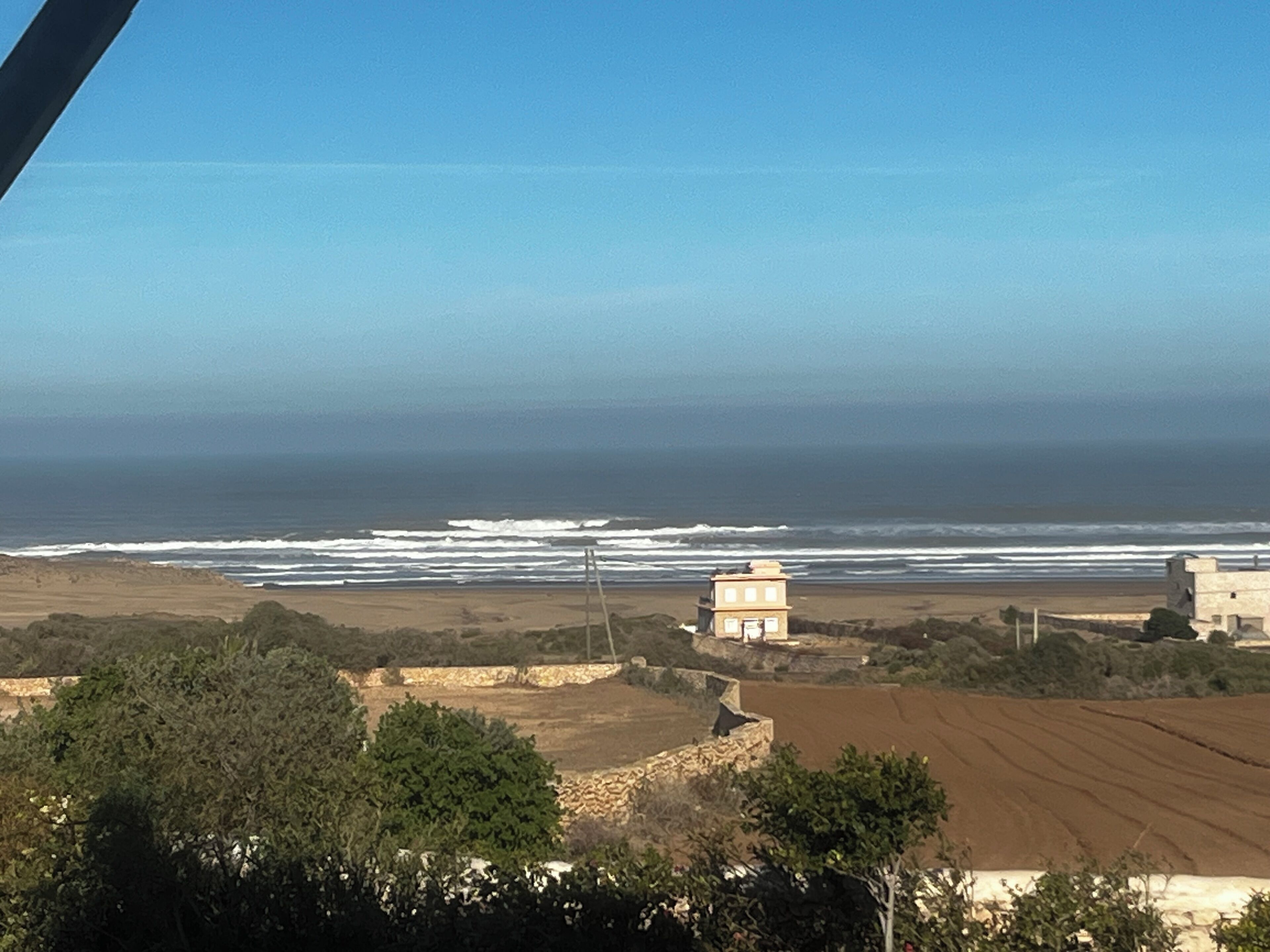 Paesaggio costiero con vista sull'oceano, un piccolo edificio e campi coltivati.
