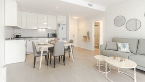 Une cuisine moderne avec des meubles blancs, une table à manger avec des chaises et un canapé gris dans l’espace salon.