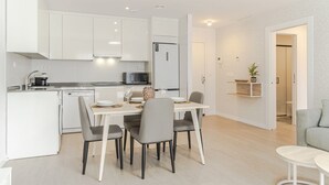 Une cuisine moderne avec des meubles blancs, une table à manger avec des chaises, un four à micro-ondes et un réfrigérateur.