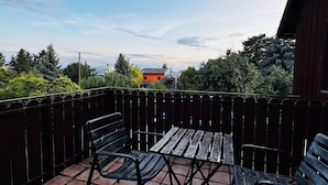 Eine Terrasse mit Tisch und zwei Stühlen, ein Holzzaun und im Hintergrund Bäume und Gebäude.