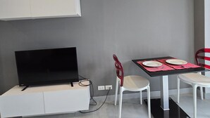 Une chambre moderne avec un téléviseur à écran plat posé sur un meuble blanc, une table à manger avec deux chaises et un set de table rouge.