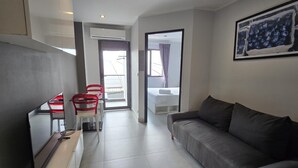 Un salon moderne avec un canapé gris, un téléviseur à écran plat et un coin repas doté de chaises rouges.