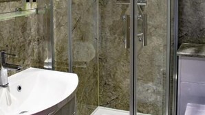 Een moderne badkamer met een douchecabine van gebogen glas, een witte wastafel en een marmeren spatwand.