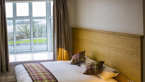 Hotelkamer met een groot bed, een houten hoofdbord, een nachtkastje met een lamp en een raam met gordijnen.
