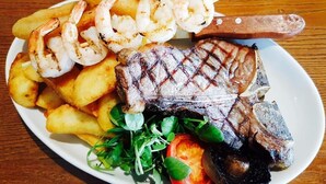 Een bord eten met gegrilde steak, garnalen, friet en een salade.