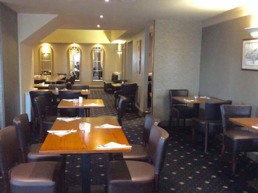 Un comedor de hotel con varias mesas y sillas, una alfombra estampada, y vista del comedor al fondo.