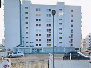 Un immeuble à plusieurs étages, doté d’une façade plate, de nombreuses fenêtres et d’un espace de stationnement où sont garées des voitures.